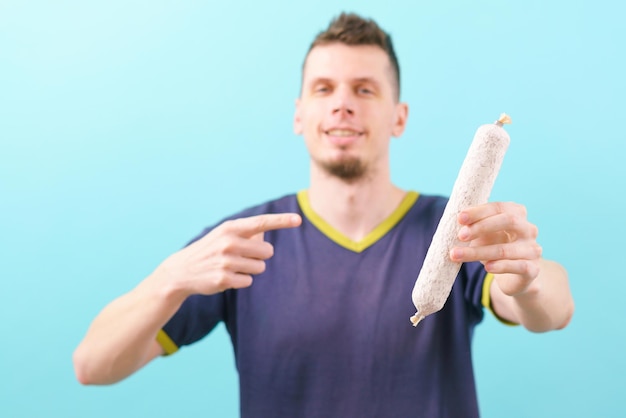 Un homme tient une saucisse de fuet blanc catalan et pointe un doigt dessus sur une coupe artisanale d'Antipasto bleu