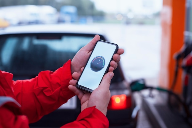 L'homme tient un smartphone avec un compteur de carburant numérique sur l'écran en arrière-plan