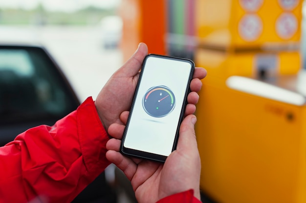 Un homme tient un smartphone avec un compteur de carburant numérique sur l'écran