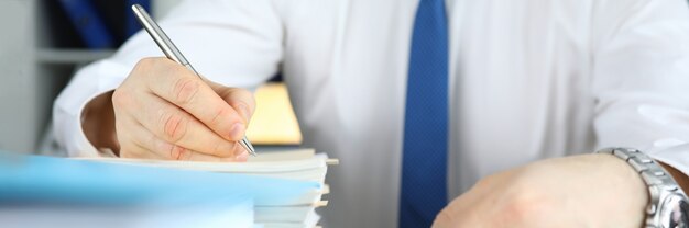 L'homme tient un stylo et écrit dans une grosse pile de documents à son bureau