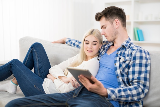 L'homme tient la tablette près de la femme sur un canapé