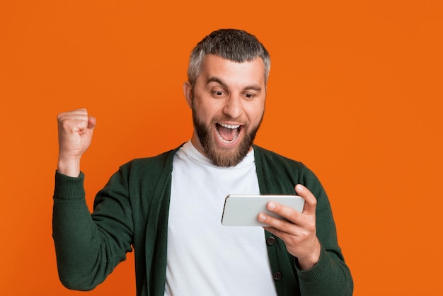 Un homme tient un téléphone intelligent moderne dans sa main droite l'écran de l'appareil éclairé il semble