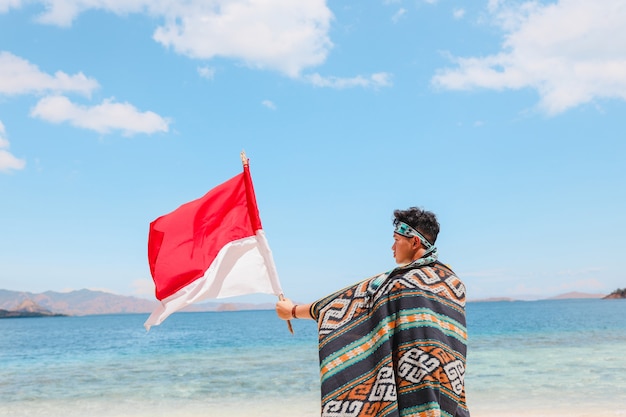 Un homme en tissu traditionnel agitant le drapeau indonésien sur la plage