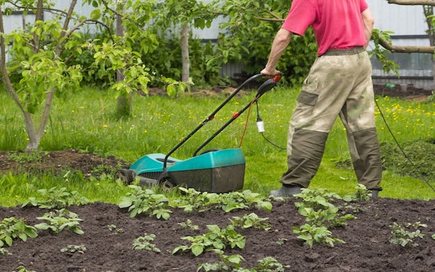 Un homme tond l'herbe avec une tondeuse à gazon électrique dans le jardin Vous pouvez voir le fil électrique