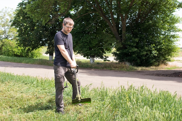 Un homme avec une tondeuse à gazon électrique tond l'herbe