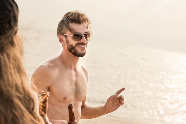 Homme torse nu avec un ami ayant parti et buvant à la plage