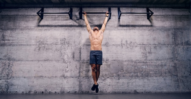 Homme torse nu faisant des tractions dans la salle de gym.