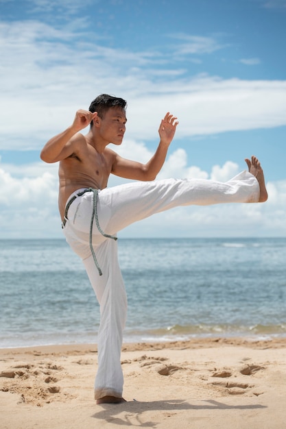 Photo homme torse nu pratiquant la capoeira sur la plage