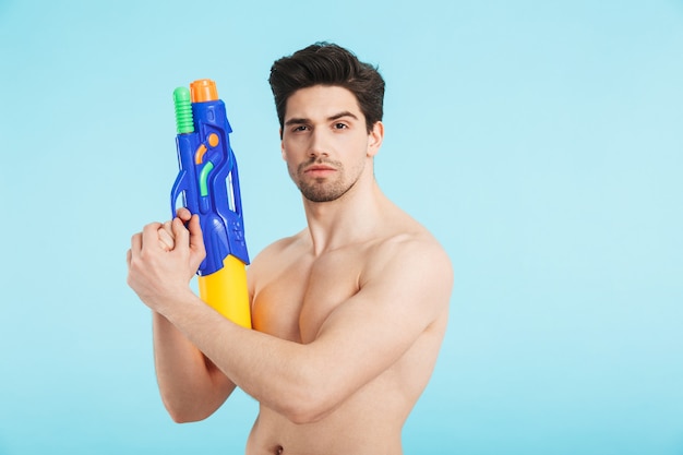 Homme torse nu sérieux debout isolé, tenant un pistolet à eau