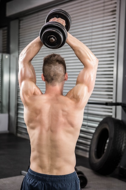 Homme torse nu, soulevant un haltère lourd au gymnase