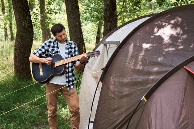 Homme de touriste avec guitare près de tente de camping
