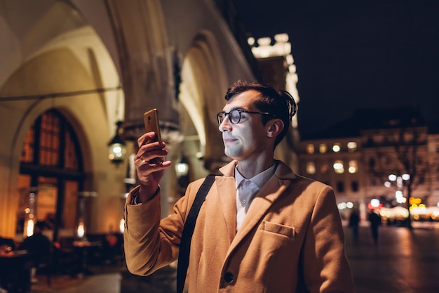 Homme touristique à l'aide de smartphone la nuit sur la place du marché à Cracovie en Pologne.