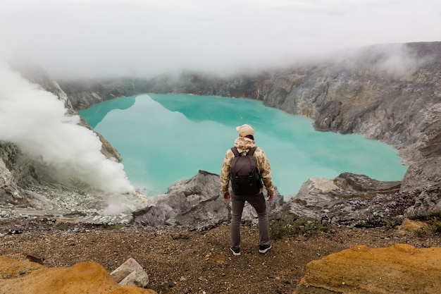 Homme touristique regarde le lac de soufre sur le volcan Ijen sur l'île de Java en Indonésie. Randonneur homme avec sac à dos voyage en haut de la montagne, concept de voyage