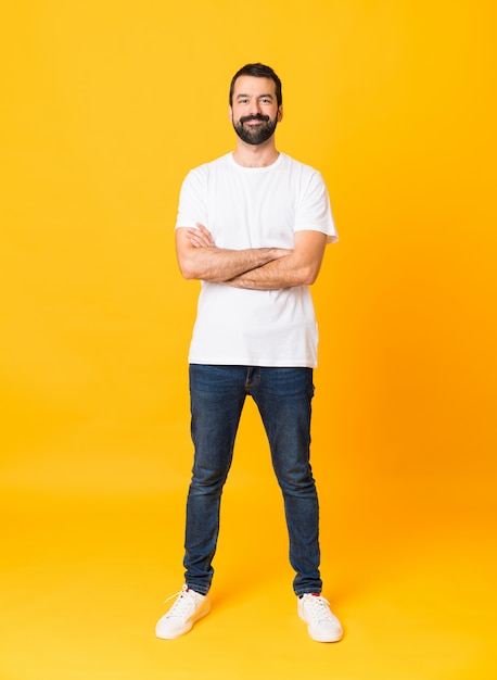 Homme de toute la longueur de la barbe sur un mur jaune isolé, gardant les bras croisés en position frontale