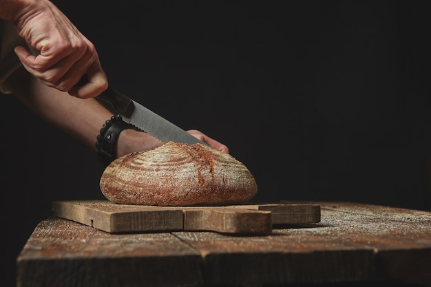 Homme trancher du pain bio frais sur une planche de bois