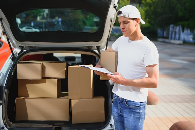 Un homme transportant un colis depuis une voiture de livraison - concept de service de messagerie