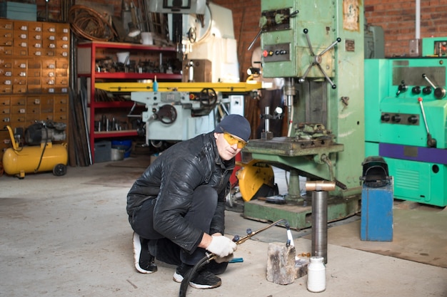 L'homme de travail est un soudeur en masque, produit métallique au garage à la maison, avec soudage au gaz brûlant à la flamme