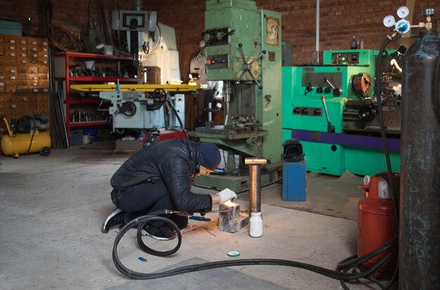 L'homme de travail est un soudeur en masque, produit métallique au garage à la maison, avec soudage au gaz brûlant à la flamme