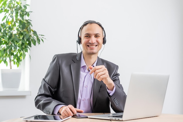 Homme travaillant au bureau de l'aube au crépuscule. Communiquer via Internet. Jeune homme d'affaires à l'aide d'un ordinateur portable tablette et d'un casque téléphonique se connectant au wi-fi. Lumière du coucher du soleil. Négociations en ligne.