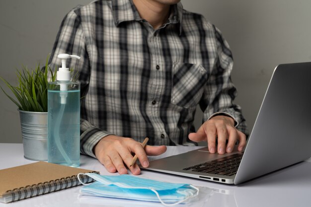 Homme travaillant devant son ordinateur portable près de masque et de désinfectant