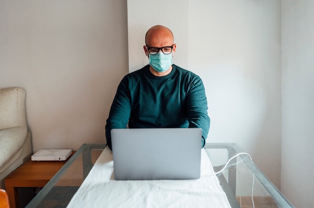 Homme travaillant à domicile sur un ordinateur portable assis à un bureau avec masque