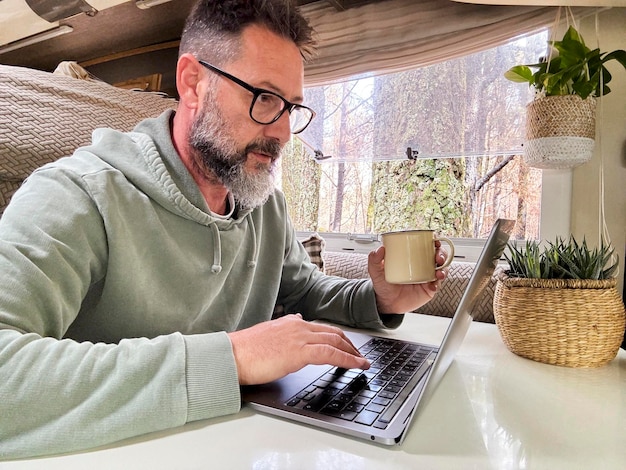 Homme travaillant à l'intérieur d'un camping-car dans une entreprise d'emploi en ligne moderne Travailleur à distance créateur de contenu influenceur vanlife concept de vie personnes Homme mature moderne utilisant l'ordinateur dans une activité de loisirs en intérieur