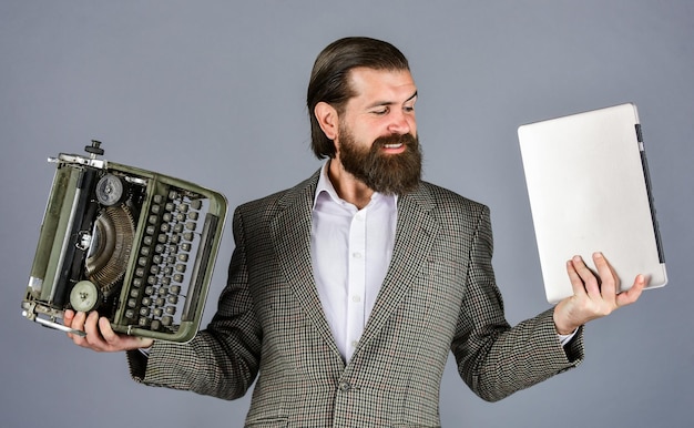 Homme travaillant sur une machine à écrire rétro dans une bibliothèque écrivain mécanique vs numérique écrit avec une machine à écrire et un ordinateur portable homme barbu en veste avec une nouvelle technologie d'écrivain de type rétro dans la vie moderne