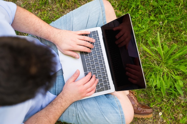 Homme travaillant avec un ordinateur portable assis dans le parc