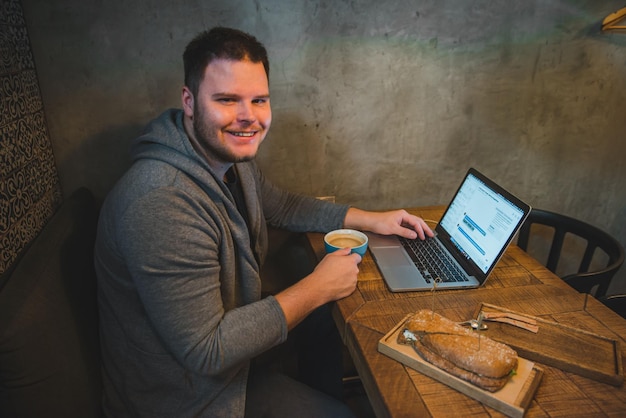 Homme travaillant sur un ordinateur portable au café petit-déjeuner sandwich et café