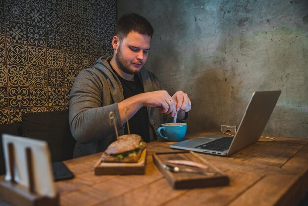 Homme travaillant sur un ordinateur portable au café petit-déjeuner sandwich et café