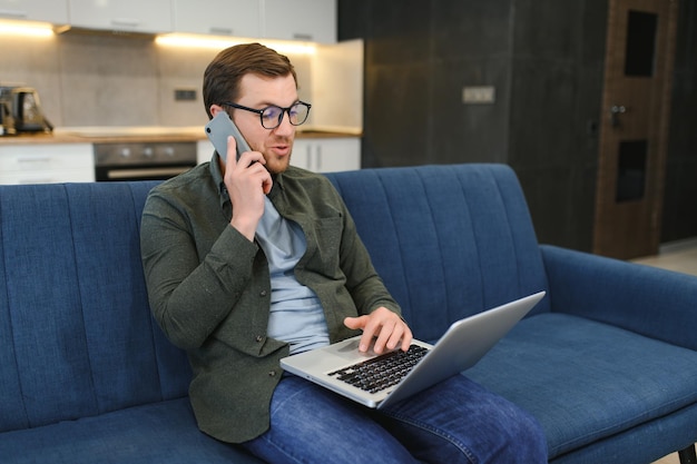 Homme travaillant sur un ordinateur portable dans sa chambre Travail à domicile ou étude concept indépendant Jeune homme assis détendu sur un canapé avec un ordinateur portable