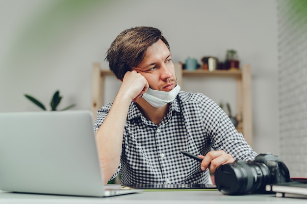 Homme travaillant sur ordinateur portable à la maison et portant un masque médical se bouchent