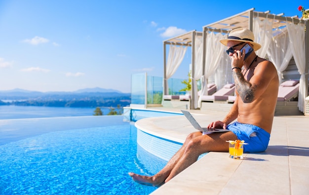 Homme travaillant pendant ses vacances parlant au téléphone et utilisant un ordinateur portable au bord de la piscine