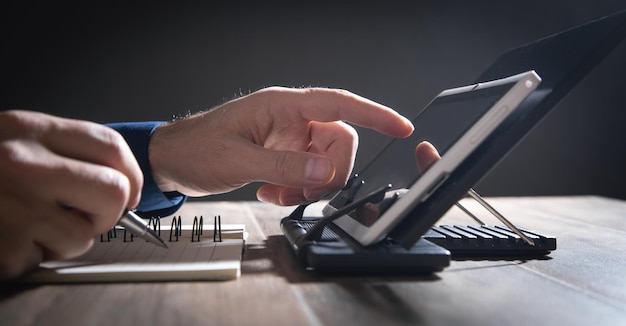 Homme travaillant sur tablette et écrit dans le bloc-notes.