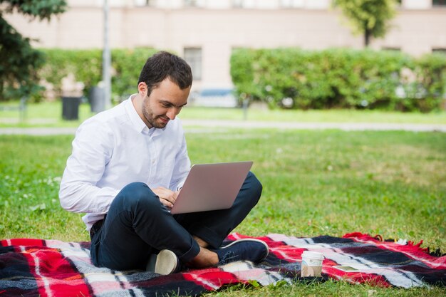 L'homme travaille à l'aide d'un ordinateur portable au parc. En plein air, le gars a l'air contesté et pense