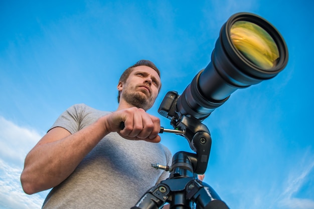 L'homme travaille avec l'appareil photo sur un trépied sur fond de ciel bleu