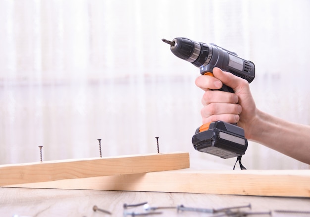 L'homme travaille avec l'assemblage de meubles à l'aide d'un tournevis électrique dans une nouvelle installation de maison - travail sur site de technicien à l'aide du concept d'outils à main