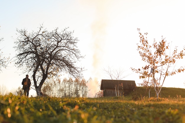 L'homme travaille dans le jardin et ramasse les feuilles d'automne dans le paysage rural pittoresque