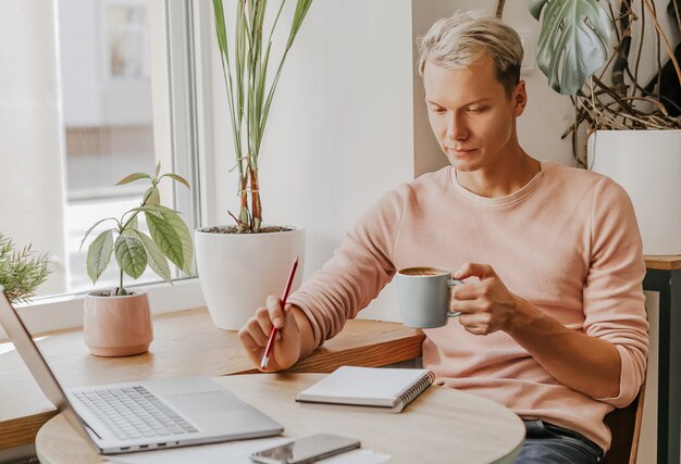 L'homme travaille sur le lieu de travail avec des documents et boit du café dans un café écologique avec des plantes