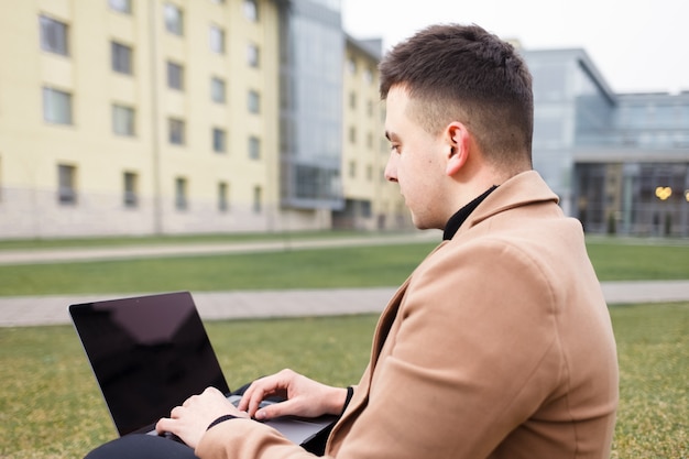 L'homme travaille sur un ordinateur portable assis sur l'herbe