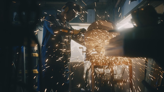 Un homme travaille avec une scie circulaire un broyeur d'ouvrier broie du métal dans l'atelier des étincelles volent du métal chaud