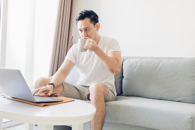 L'homme travaille sur son ordinateur portable dans le salon avec une tasse de café.