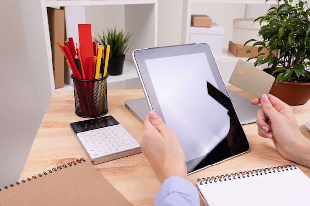 Un homme travaille avec une tablette et prend des notes sur son bureau avec une calculatrice, des stylos, des crayons, une carte, un téléphone et une plante au bureau