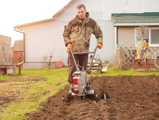 Un homme travaille la terre dans le jardin avec un cultivateur prépare le sol pour semer le concept d'agriculture