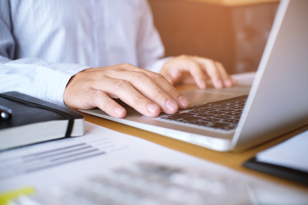 L&#39;homme travaille en utilisant un ordinateur portable sur une table en bois. Mains tapant sur un clavier