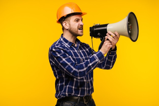 Homme travailleur en colère en casque orange avec un mégaphone sur jaune