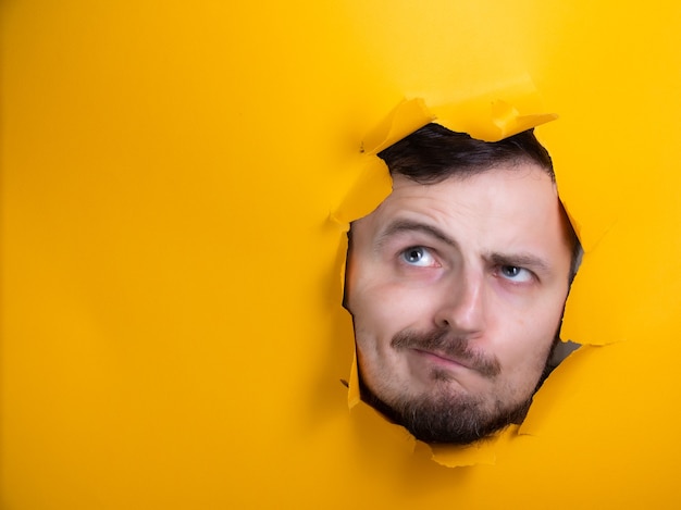 Homme à travers un trou papier jaune pensant