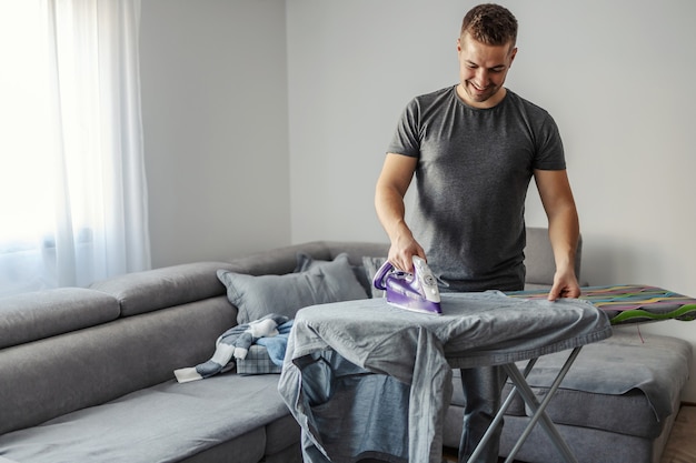 Un homme d'une trentaine d'années repassait des vêtements sur une planche à repasser dans le salon