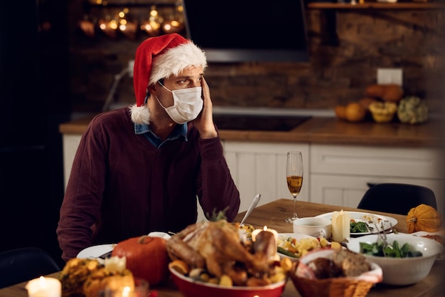 Homme triste avec masque facial assis seul à table à manger à Noël en raison de la pandémie de COVID19