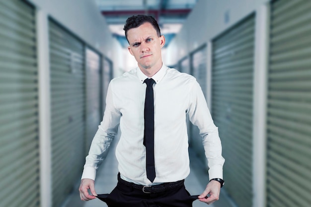 Un homme triste montre un pantalon de poche vide près d'un magasin fermé